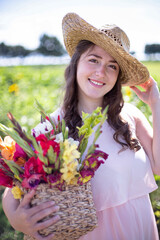 White young woman with long hair in light dress with a basket of colorful flowers in the countryside portrait