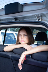 Portrait of dark blond slim young woman in open car trunk behind the seats