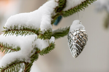 A shiny silver color Christmas ornament hanging from a pine tree with snow