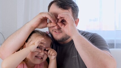 funny Little daughter 3 years old and father are having fun at home, making funny faces, making glasses with their fingers, like glasses looking at the camera through binoculars. have fun with kid