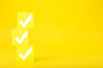 Three white checkmarks on yellow toy cubes against bright yellow background with copy space