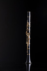 A full size clarinet with gold plated keys on a reflective surface and a black background. A woodwind instrument common to classical music.