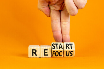 Refocus and restart symbol. Businessman turns cubes and changes the word 'refocus' to 'restart'. Beautiful orange table, orange background. Business refocus and restart concept. Copy space.