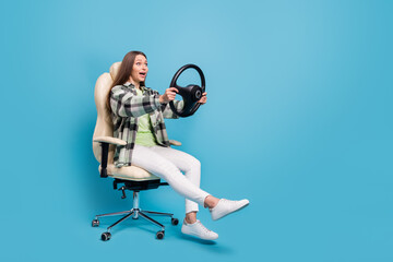Full length profile side photo of young girl sit chair hold steering-wheel amazed shocked speed isolated over blue color background