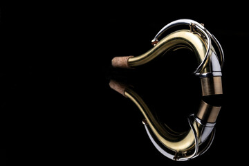The neck of a saxophone on a reflective surface and a black background
