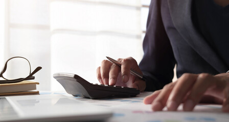 Fototapeta premium Close up of businessman or accountant hand holding pen working on calculator to calculate business data, accountancy document and laptop computer at office, business concept