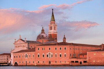 Fototapeta premium Romantic Venetian architecture at sunset. Church of San Giorgio Maggiore on San Giorgio island in Venice, Italy. Calm sea water and gorgeous orange and pink sunset clouds.