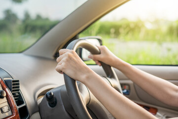 Hand female on the steering wheel of a car while driving the windshield and road. Close up of woman hand holding steering wheel on her car.