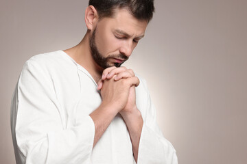Religious man with clasped hands praying against grey background. Space for text