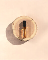 Glass perfume sample with brown liquid on a wooden tray lying on a beige background. Luxury and natural cosmetics presentation. Tester on a woodcut in the sunlight. Top view