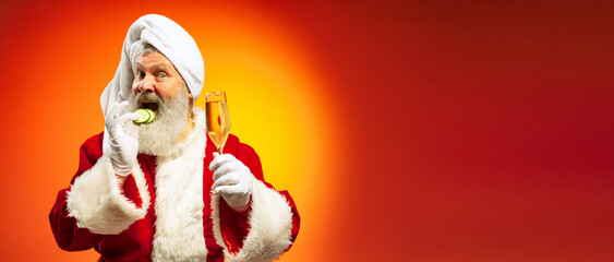 Funny senior man wearing white towl and costume of Santa Claus congrats everybody with New Year 2022 isolated on red yellow background in neon.