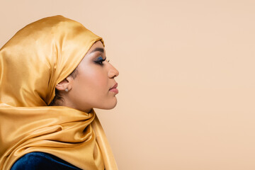 profile of muslim woman in yellow hijab with bright makeup isolated on beige