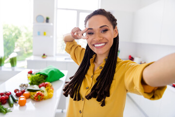 Photo of excited cute dark skin lady wear yellow shirt recording video v-sign cover eye indoors room home house