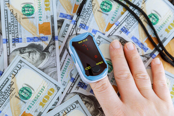 Pulse oximeter on fingers. Measurement of oxygen in the blood on the table near the dollars.