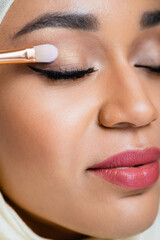 close up of muslim woman with closed eyes applying eye shadow with cosmetic brush