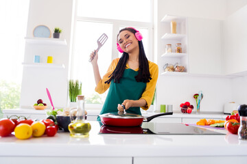 Photo of cute shiny dark skin lady wear yellow shirt headphones cooking frying indoors room home house