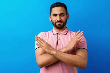 Arabian handsome man keeping arms crossed, rejecting against blue background