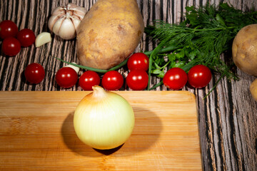 Fresh onion bulbs, not peeled on a wooden board, next to vegetables