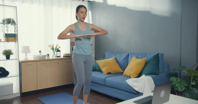 Young attractive Asia woman in sportswear watching fitness online video on laptop practice yoga for beginner in living room at house. Home quarantine workout and fitness exercise without the gym.