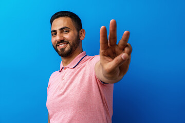 Young arabian man smiling and showing three fingers against blue background