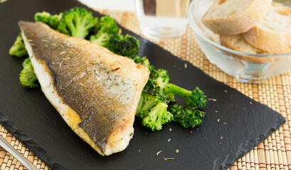 fried fillet of sea bass with garnish of broccoli on black warm stone plate