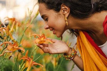 Young indian woman wearing sari smiling while smelling flower