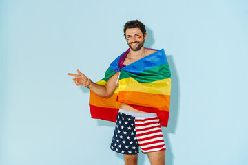 Young man with rainbow flag smiling while pointing finger aside