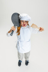 High angle view of little cute girl in white cook uniform and huge chef's hat posing isolated on...