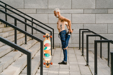 Shirtless man doing warmup while standing with skateboard on stairs - obrazy, fototapety, plakaty