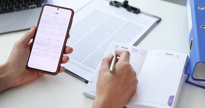 Woman holds smartphone with calendar for 2022 and makes business plan for next year 4k movie