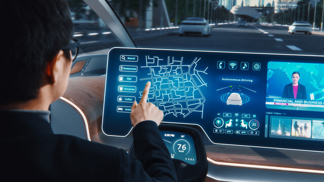 Futuristic Concept: Stylish Businessman Setting Location on an Interactive Navigation App on an Augmented Reality Dashboard while Sitting in an Autonomous Self-Driving Zero-Emissions Electric Car. 