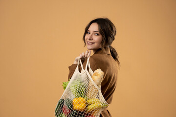 Young woman holding mesh grocery bag with vegetables Concept of no plastic. Zero waste, plastic...