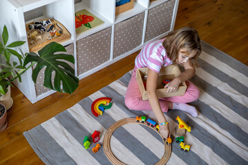 Child rolls a steam locomotive on a wooden railroad. Montessori material.