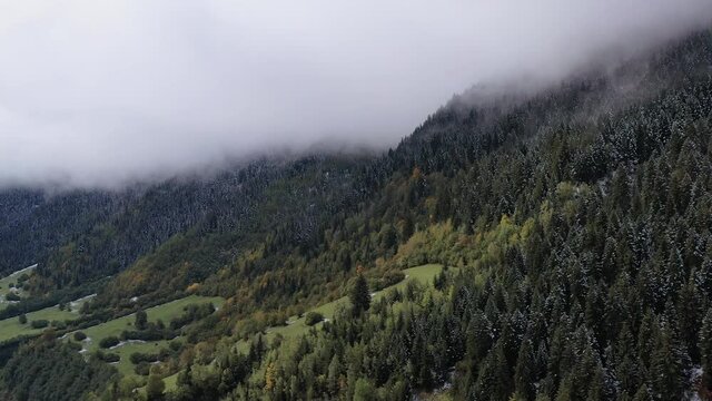 Aerial view of the forest in the mountains. Amazing landscape. Beautiful autumn trees covered with clouds. The trees are hidden in the clouds. Snow on the trees. 4K drone video. Caucasus mountains.