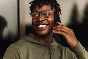 Smiling african american man, wearing glasses talking on phone outdoors outdoors enjoying mobile conversation