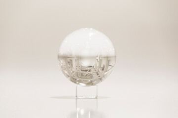 A glass or crystal sphere on a glass stand on the floor in a white room
