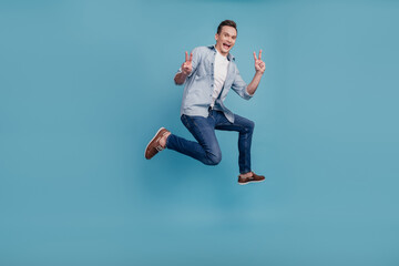 Fototapeta na wymiar Full body profile side photo of young man have fun jump runner show peace v-sign isolated over blue color background