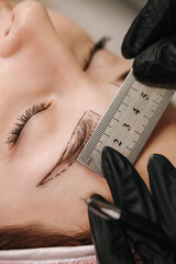 Close-up of the girl's face with closed eyes. The hand of the master holds a metal ruler over the...