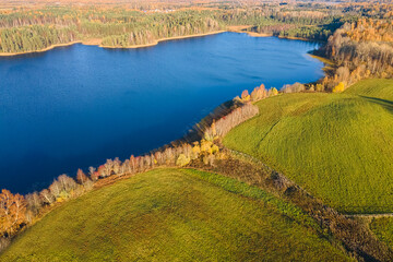 A green field and a cold blue lake. Autumn landscape shooting from the air. It can be used as wallpaper and for advertising.