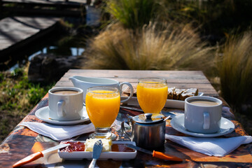 delicioso desayuno campestre al aire libre, sobre una mesa de madera en el jardin, cafe, jugo de...