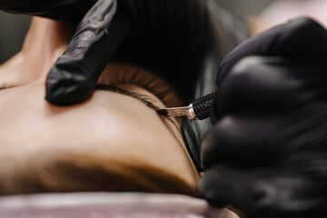 Fototapeta premium eyebrow microblading. A master in black gloves holds a blending needle over the brow of the model. Macro photography