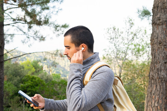 Young ethnic man using smartphone and true wireless earphones in woods - Powered by Adobe