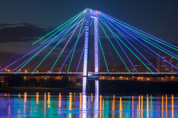 Fototapeta na wymiar Beautiful view of a bright and colorful bridge across the river. Cityscape at night with a beautiful bridge over the river