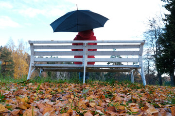 A Woman in a Red Jacket Is Sitting on a White Bench in the Park