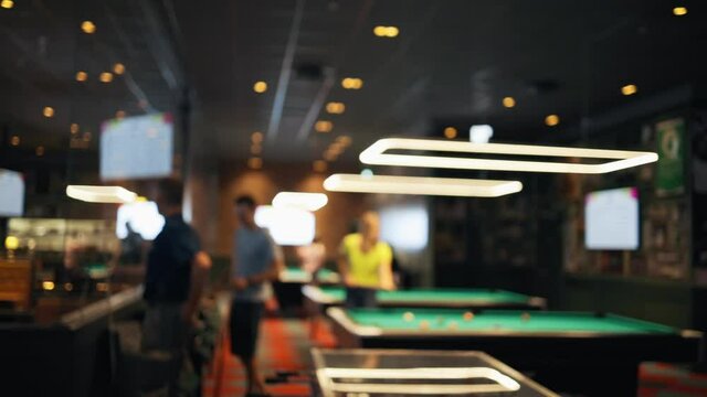 Defocused group of people playing pool or billiards in bar or pub after pandemic