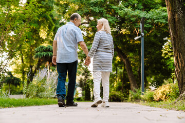 White senior couple holding hands and smiling while walking in park