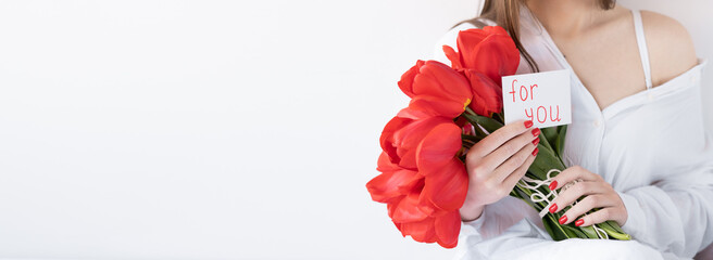Girl with red flowers on a white background. Tulips and a postcard for you in hand. Banner.