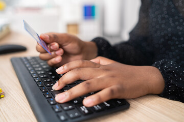 Black keyboard from computer, desk in office, secretary, woman employee tapping fingers on keys, female dark skinned hands, holding bank card, shopping paying online