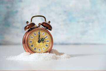 Vintage alarm clock in artificial snow showing clock change to winter time, light blue background with copy space, selected focus, narrow depth of field