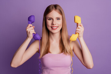Portrait of positive secretary lady hold two landline telephone wear pink top on violet background